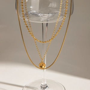 Detail of layered gold necklace with bead chain and round pendant on a glass