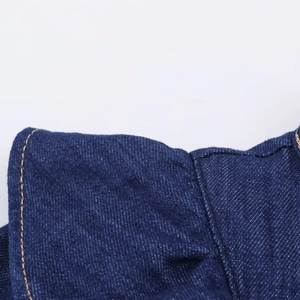 Détail du tissu denim bleu montrant la texture sergée et les coutures jaunes du costume