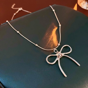 Macro shot of silver bow pendant on delicate snake chain with small bead accents