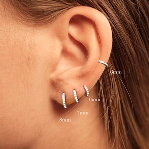 Model wearing 6mm, 7mm, and 8mm silver crystal huggie hoop earrings on different ear parts