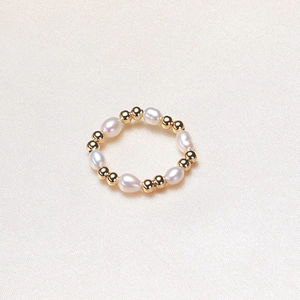 Elastic freshwater pearl ring with gold beads on elegant silk fabric background