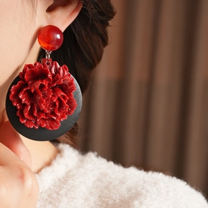 Gros plan d'une boucle d'oreille fleurie avec pétales rouges et disque noir sur modèle