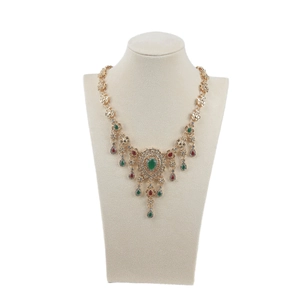 Vintage gold necklace with red and green teardrop gems on a beige velvet bust stand