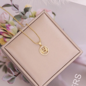 Macro detail of 18K gold-plated zodiac pendant with micro-pave crystals on a gift box