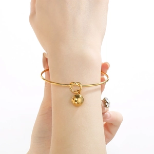 Minimalist gold knot open bangle with hollow sphere charm on woman's wrist
