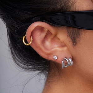 Close-up of triple layered earrings set featuring gold and silver metal textures on ear