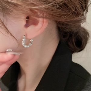 Silver C-shaped hoop earrings with pearls and crystals worn by a female model