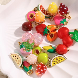 Detail of diverse fruit enamel charms including cherry and strawberry on a shell tray