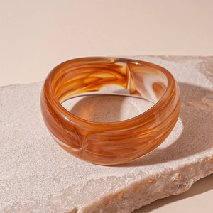 Macro shot of wide amber resin bangle with marble texture on a stone surface