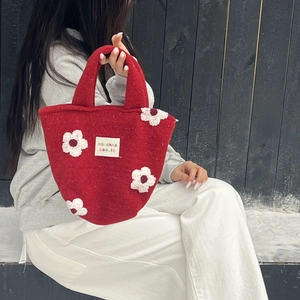 Detail of red felt tote bag featuring 3D white floral patches and woven logo label