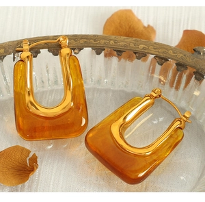 Close-up of amber U-shaped resin earrings with golden metal clasps on textured glass