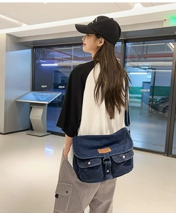 Vue latérale d'un sac bandoulière en denim bleu foncé avec étiquette en cuir sur mannequin