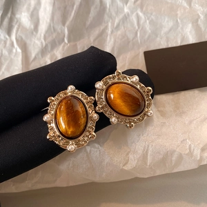Gros plan de boucles d'oreilles dorées avec œil de tigre ovale et bordure en perles