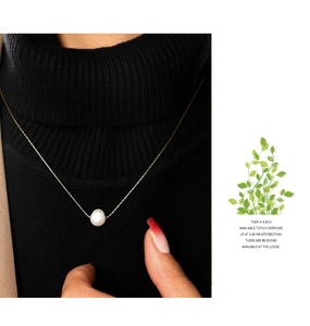 Minimalist single pearl pendant necklace on gold chain worn over a black sweater
