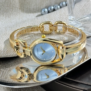 Close-up of golden horseshoe watch with blue dial and metallic bracelet on elegant tray
