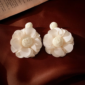 Détail de boucles d'oreilles fleurs en dentelle blanc crème sur velours foncé