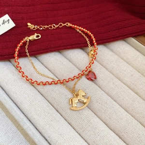Detail of gold plated double-layer bracelet with red heart charm and rocking horse