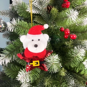 Plush Christmas bear ornament with sequins hanging on a green tree branch with red berries