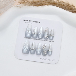 Faux ongles dégradé bleu avec nœuds 3D et strass présentés sur un plateau blanc