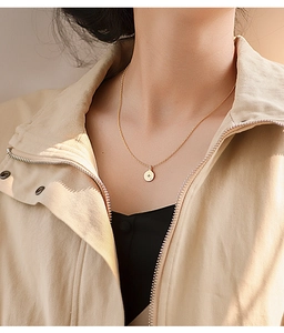 Close-up of a gold coin necklace with a star engraving worn on a model's neck