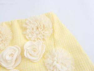 Dettaglio di gonna in tweed a quadri gialli con fiori 3D in tessuto bianco e trama