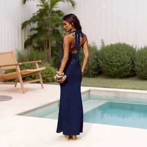 Navy blue lace evening gown with a backless halter neck design in a poolside setting