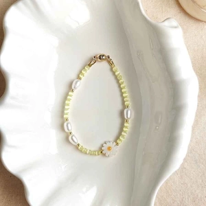 Detail of floral beaded bracelet with white daisy charm and gold magnetic clasp on shell plate