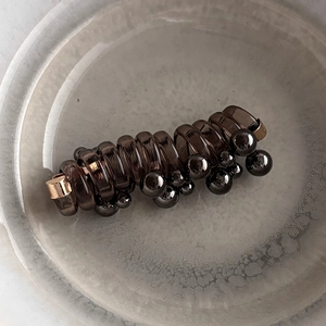 Macro detail of dark brown spiral hair coil with metallic beads on a ceramic plate