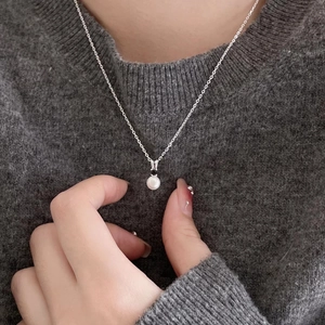 Detail of 925 silver necklace featuring a white pearl pendant and black stone on a model