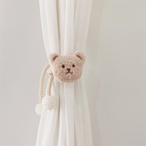 Close-up of a plush bear curtain tieback in beige with woven rope and pearl buckle detail