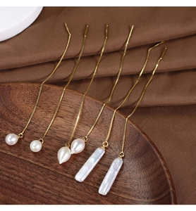 Macro detail of gold-plated silver thread earrings with white pearls on a silk tray