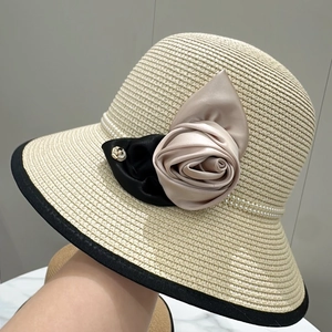Détail du chapeau de paille avec rose en satin, nœud noir et perles sur tissage beige