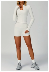 Close-up of white ribbed yoga set featuring long sleeve zip jacket and high waist shorts