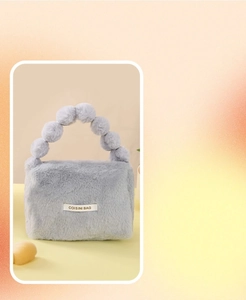 Close-up of a grey plush handbag with a unique spherical pom-pom handle and white label