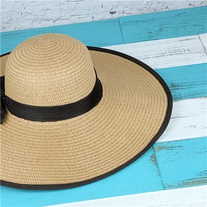 Detail of woven straw sun hat with wide black grosgrain ribbon and bow on wooden background