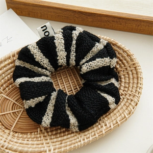 Detail of a black and white striped tweed scrunchie with a small label on a woven tray