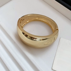 Detail of wide polished gold oval bangle with mirror finish and side hinge mechanism