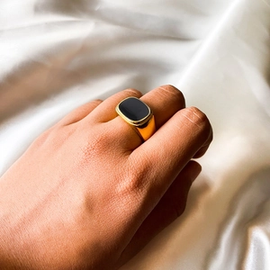 Gros plan d'une bague chevalière dorée avec insert noir portée sur de la soie blanche