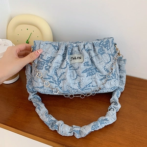 Blue pleated shoulder bag with floral silver chain and textured fabric on wooden table