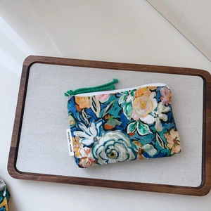 Detailed macro view of a floral cotton makeup bag with green woven zipper pull on a tray