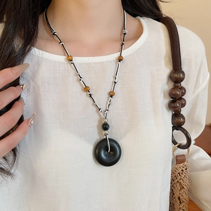 Close-up of ethnic cord necklace with black circular pendant and brown wood beads on a model