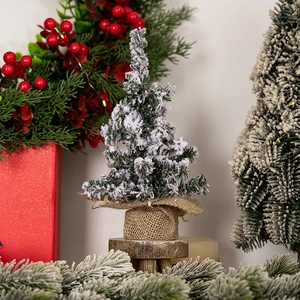 Close-up of a mini snowy Christmas tree with a burlap base and wooden stand on a festive table