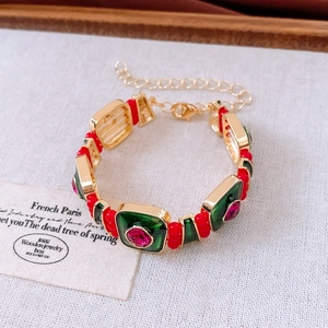 Dettaglio di un bracciale vintage dorato con smalto verde e gemme rosse su tessuto bianco