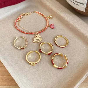 Gold-plated ring set and bracelet with red enamel accents on a textured tray