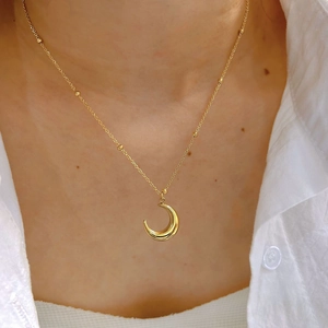 Elegant gold crescent moon pendant necklace with small bead chain on a white linen shirt