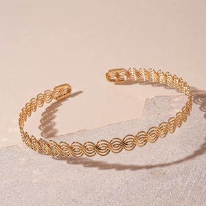 Detail of a wavy hollow gold-plated open bangle on a grey textured stone block