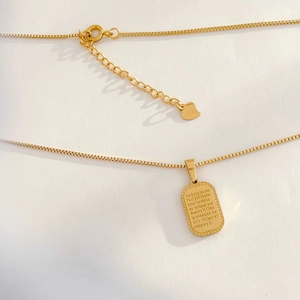 Detail of gold box chain necklace with a rectangular engraved pendant and heart charm