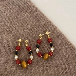 Tiger eye and pearl beaded hoop earrings with red beads on brown knit fabric texture