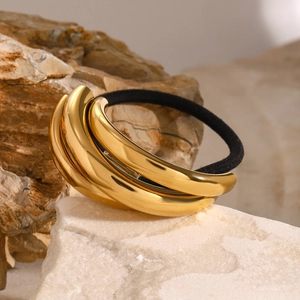 Close-up of polished gold stainless steel hair tie on a beige stone background