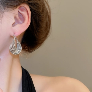 Close-up of a silver multi-layered hollow twisted oval hoop earring on model's ear